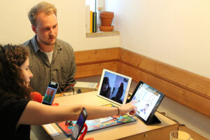Zwei Studierende sitzen am Tisch mit Tablet und Spielebrett